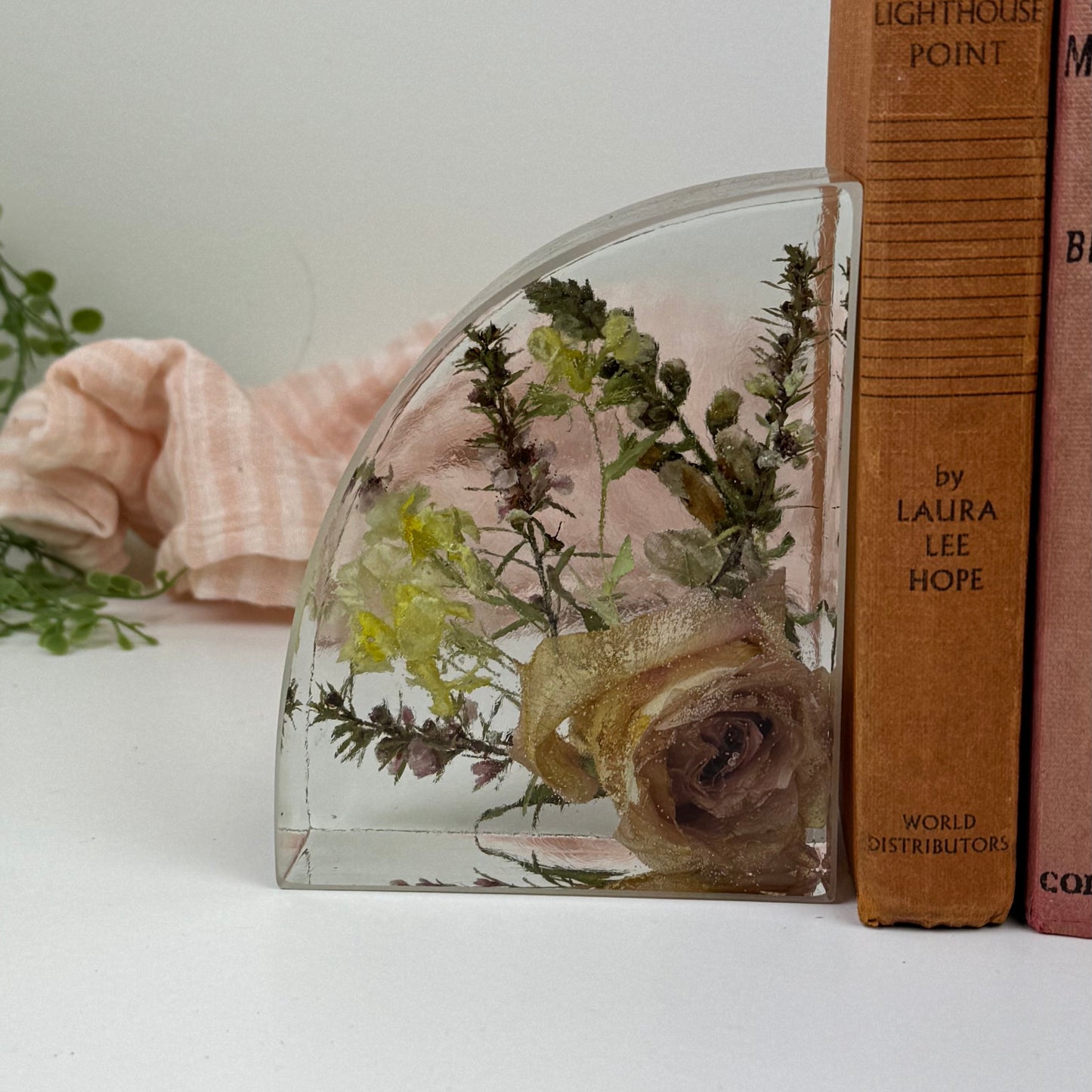 Glass bookend with preserved flowers next to a stack of books on a white surface.